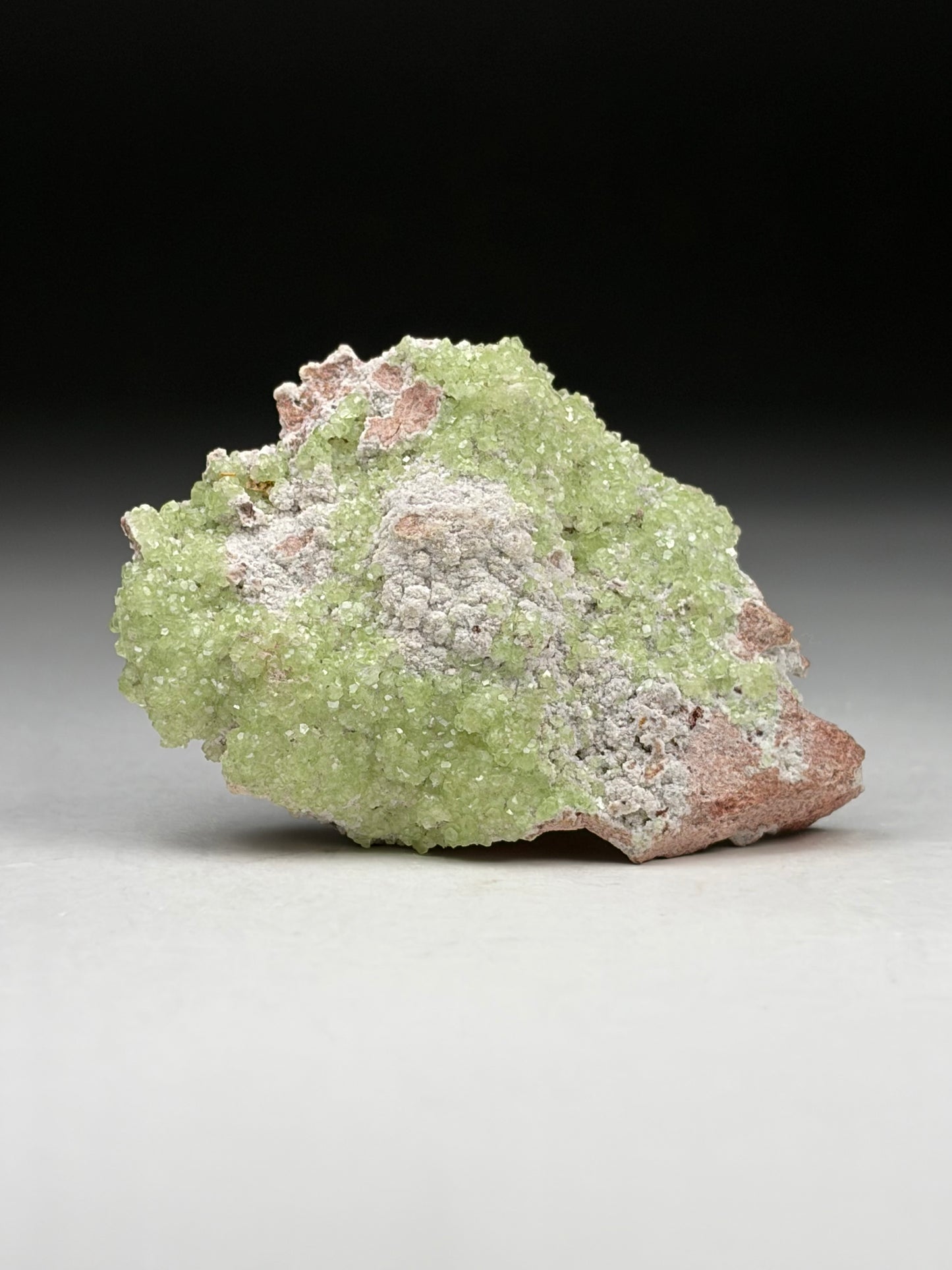 Green mineral specimen on a gray surface with a black background