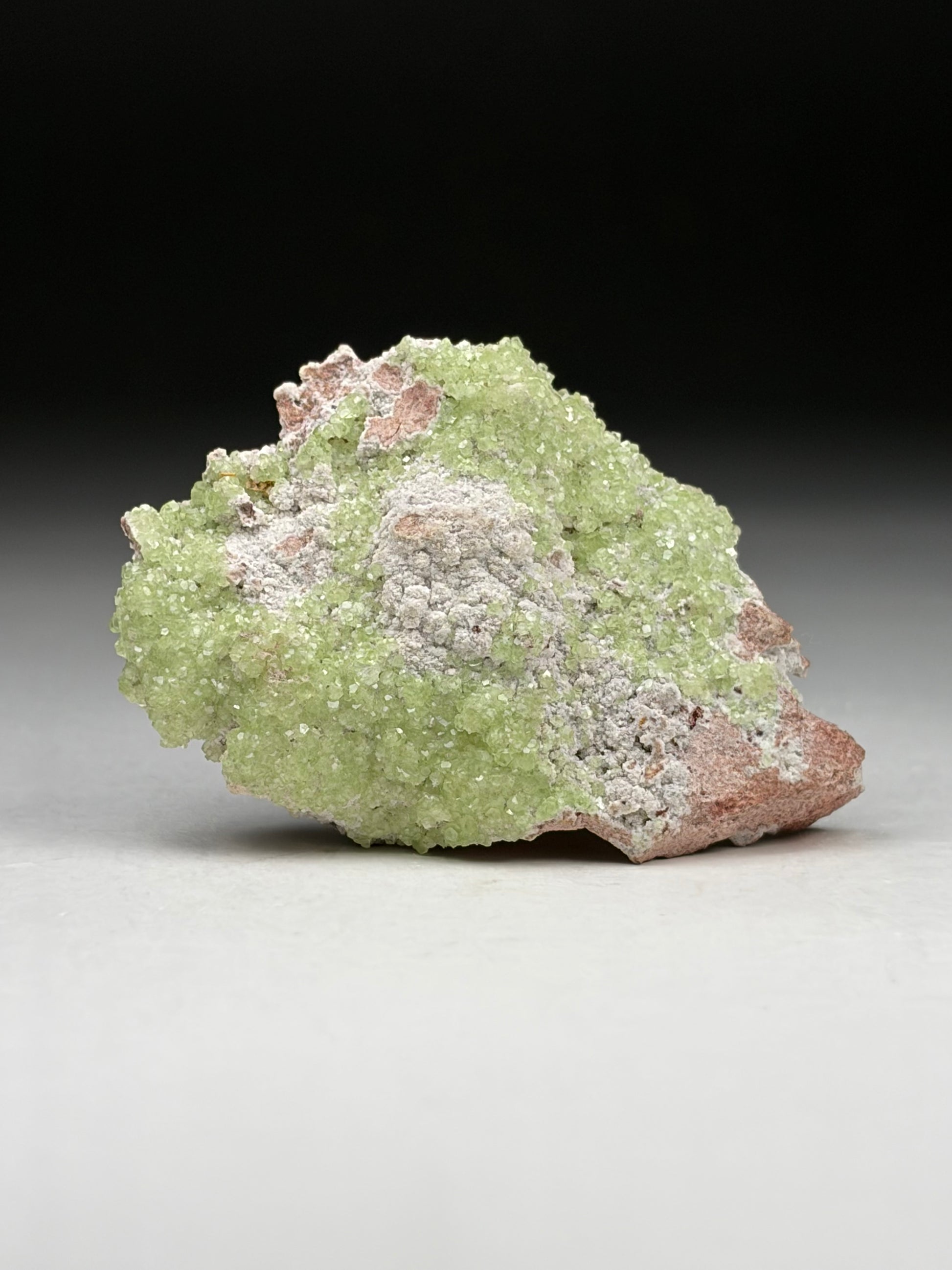 Green mineral specimen on a gray surface with a black background