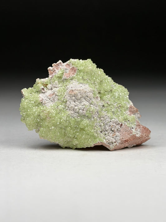 Green mineral specimen on a gray surface with a black background